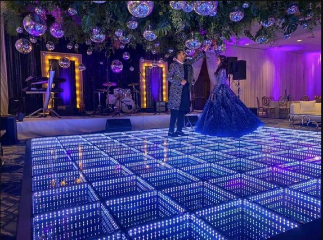Couple sharing a first dance on a white infinity LED dance floor beneath suspended mirror balls