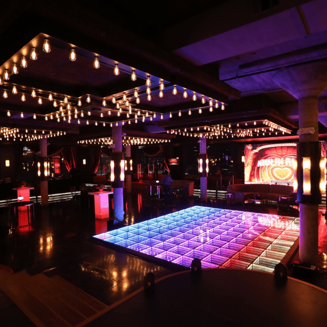 Red and pink LED dance floor under strings of edison bulbs at a lounge takeover