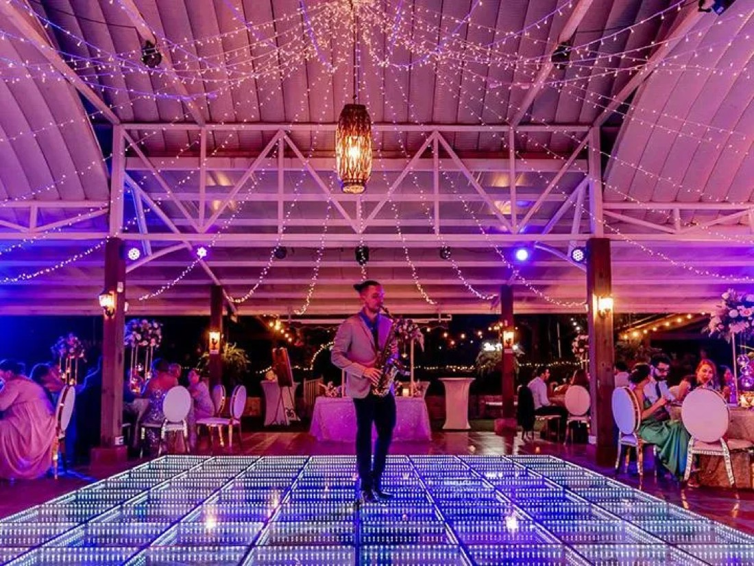 Saxophonist performing on an infinity LED dance floor beneath string lights at an evening celebration